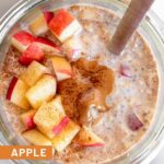 Apple cinnamon overnight oats in a jar topped with diced apples, peanut butter, and cinnamon and a spoon in the jar.
