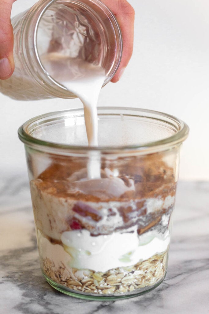 Jar filled with oats, yogurt, and fruit with milk being poured into it.