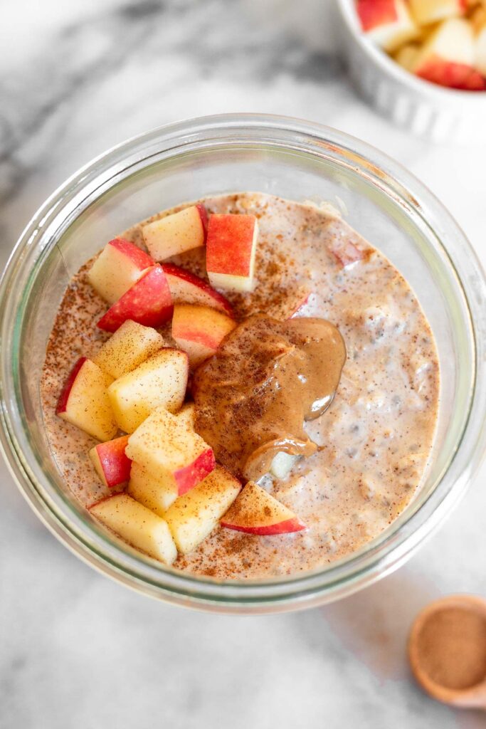 Apple overnight oats in a jar topped with diced apples, peanut butter, and cinnamon.