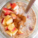 Apple cinnamon overnight oats in a jar topped with diced apples, peanut butter, and cinnamon and a spoon in the jar.