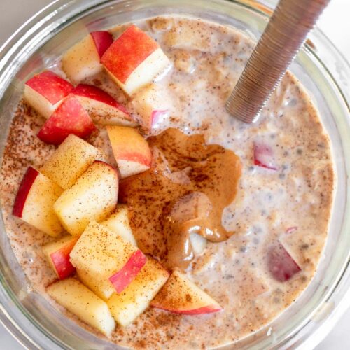 Apple cinnamon overnight oats in a jar topped with diced apples, peanut butter, and cinnamon and a spoon in the jar.