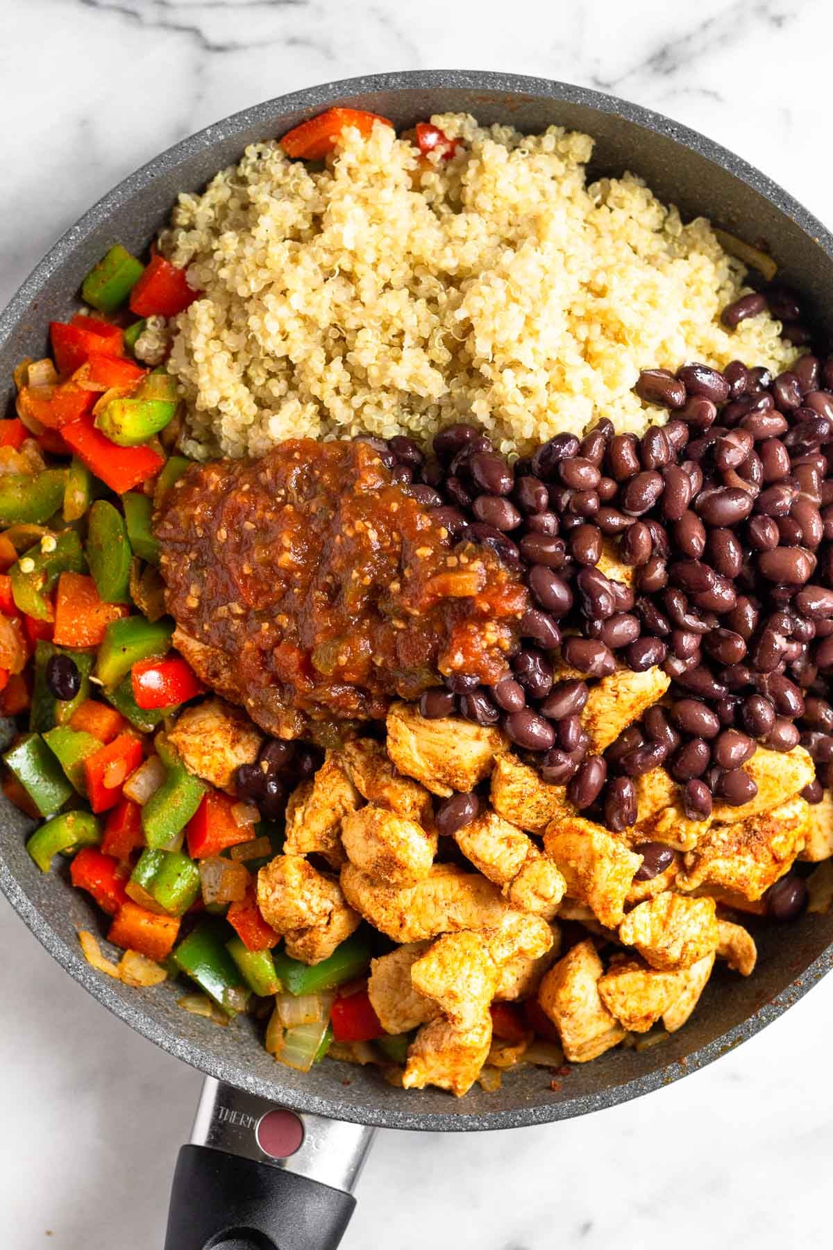 Skillet filled with piles sautéed veggies, quinoa, black beans, sautéed chicken, and salsa.