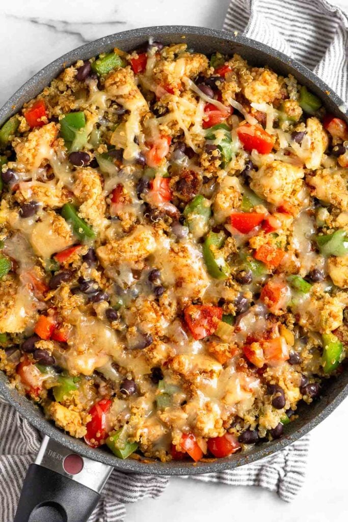 Large pan filled with chicken, veggies, quinoa, and beans topped with melted cheese.
