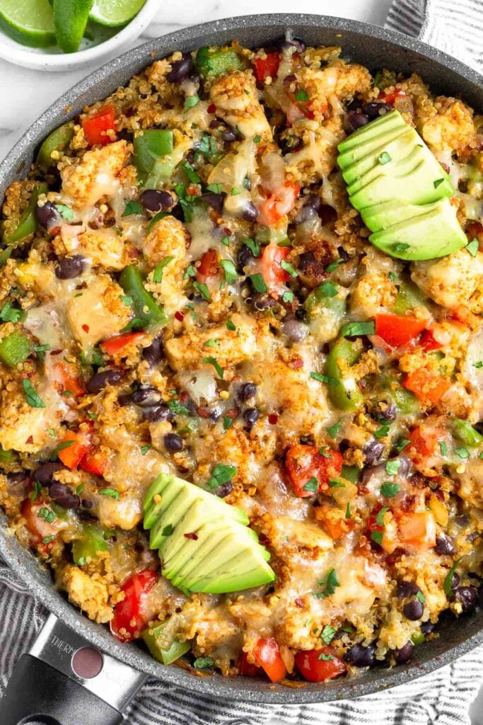 Chicken and quinoa skillet with veggie and cheese topped with avocado and cilantro.