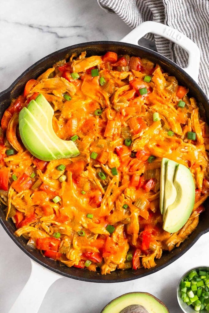 Buffalo chicken casserole topped with melted cheese, avocado, and green onion in a large cast iron.