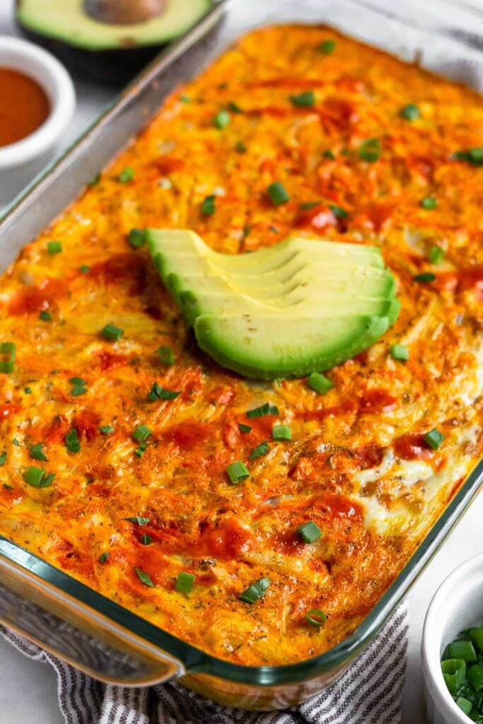 Egg casserole with chicken and veggies in a casserole dish. It is topped with avocado, hot sauce, and green onion.