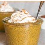 Jar of pumpkin chia pudding topped with whipped cream and cinnamon. A spoon is coming out of the jar and another jar is behind it.