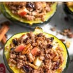 Baking sheet filled with stuffed acorn squash with the filling scattered around it as to make it look like they are overflowing. Two cinnamon sticks are on the baking sheet as well.