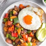 Chicken hash on a plate topped with a fried egg and avocado.