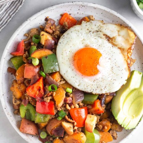 Chicken hash on a plate topped with a fried egg and avocado.