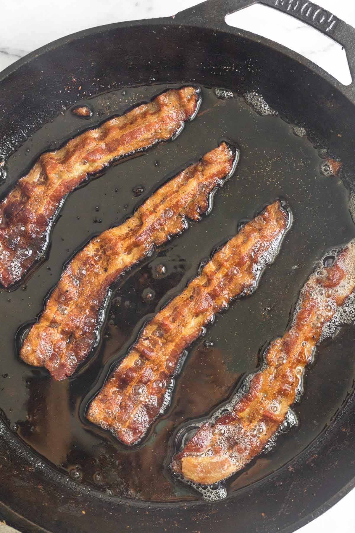 Cast iron skillet with four pieces of cooked bacon in it.