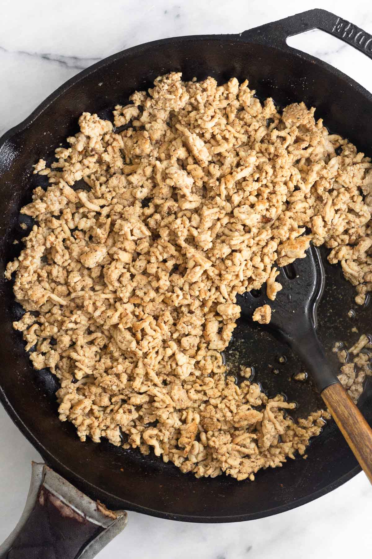 Cast iron skillet filled with browned ground chicken with a spatula in it.