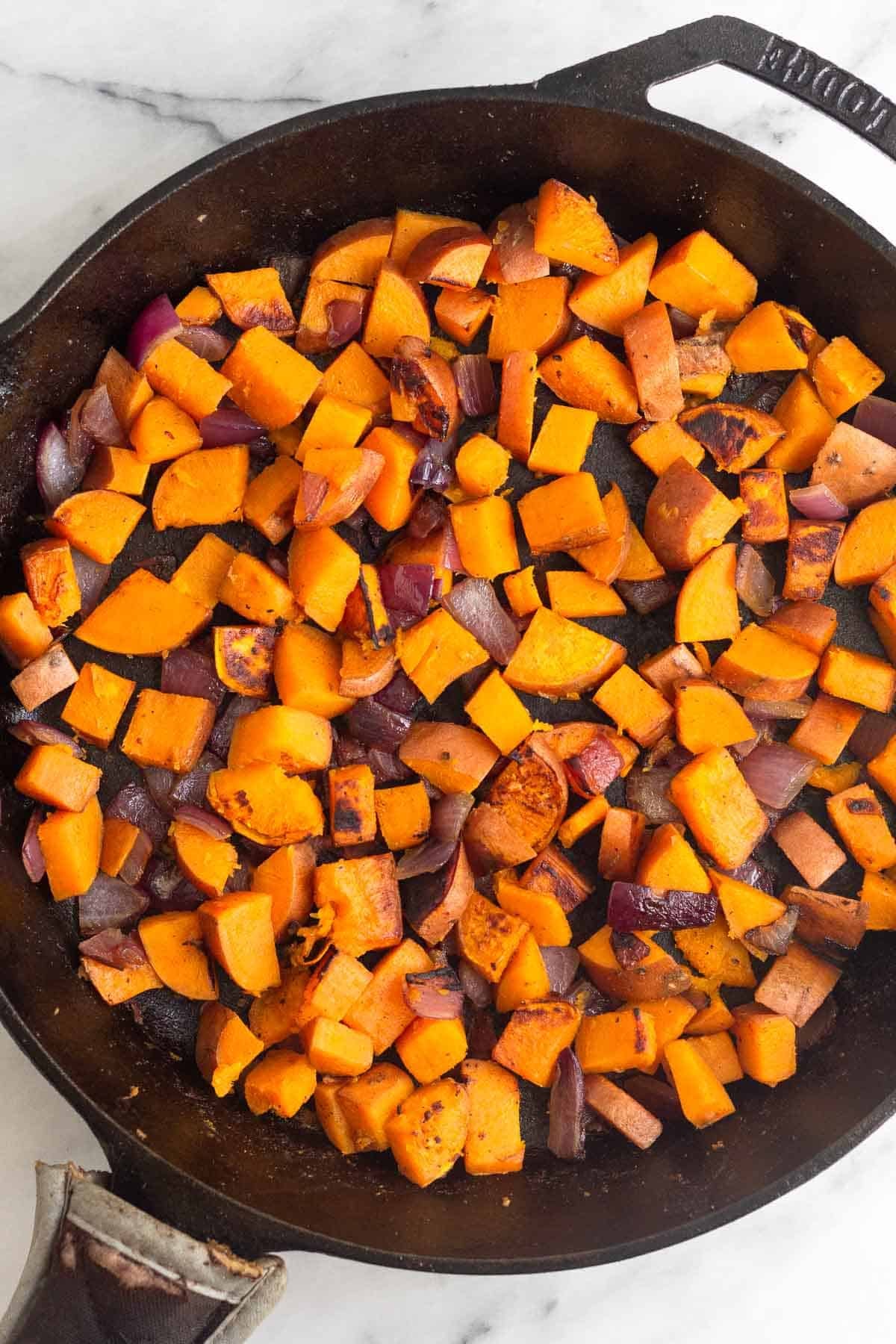 Cast iron skillet filled with sautéed sweet potatoes.