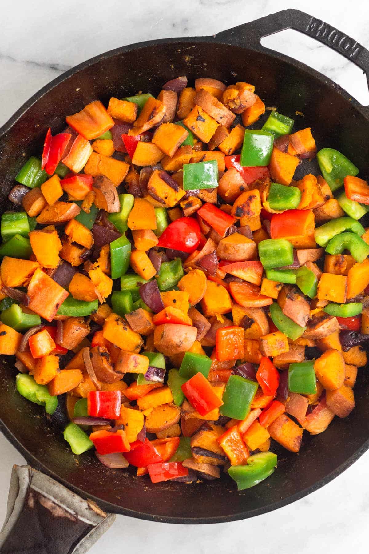 Cast iron skillet filled with sautéed sweet potatoes and peppers.