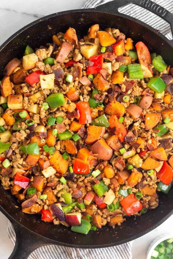 Overhead shot of chicken hash with sweet potatoes and veggies in a large cast iron skillet.