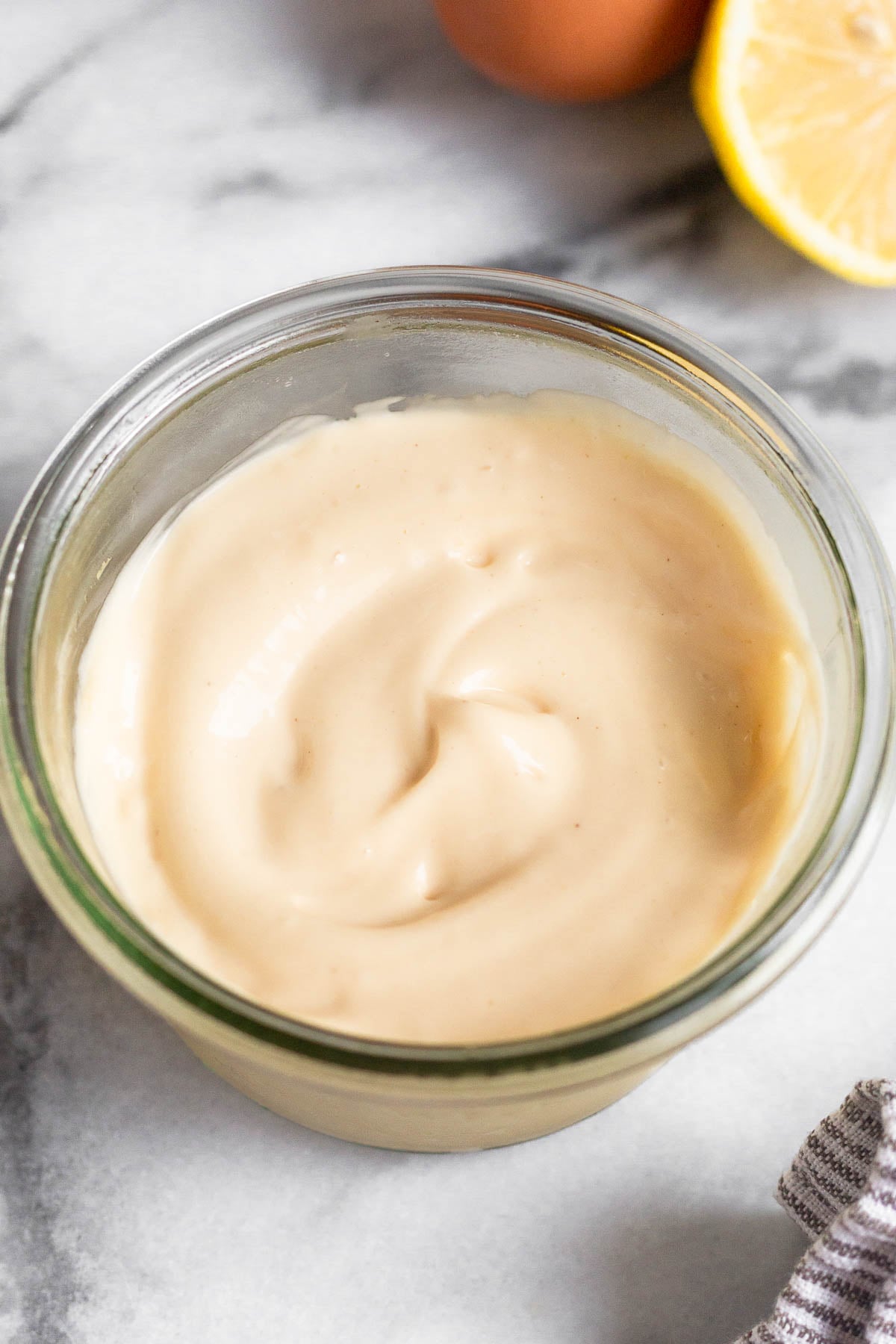 Homemade mayo in a jar with half a lemon and an egg next to it.