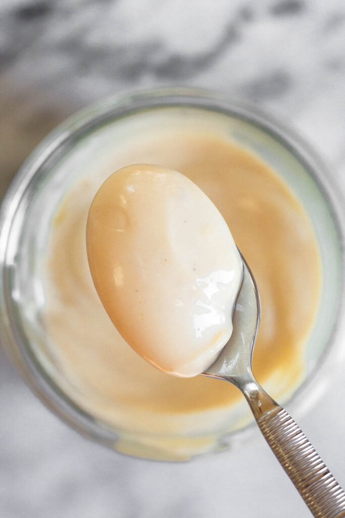 A spoonful of homemade mayo being scooped out of a small jar.