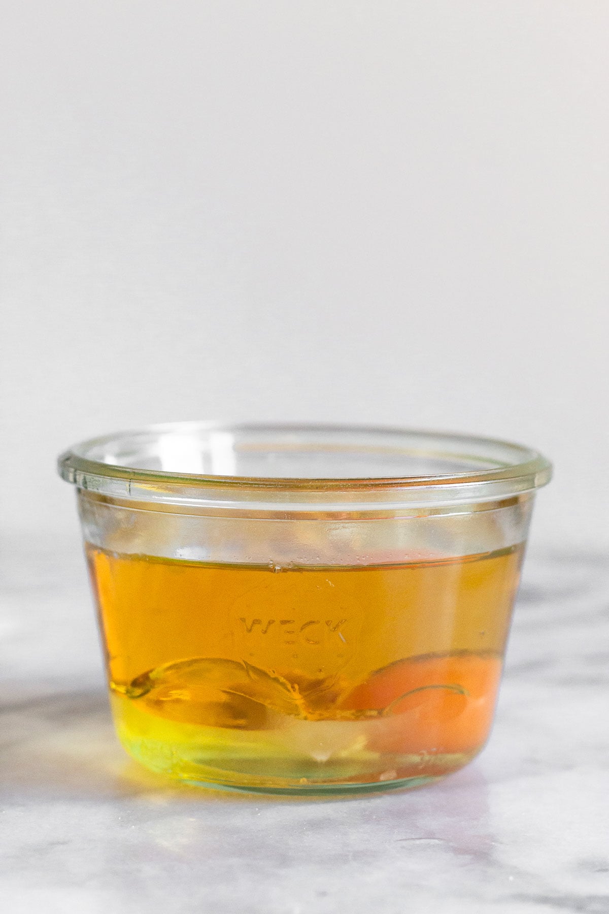 A small jar filled with a raw egg, oil, and some spices.