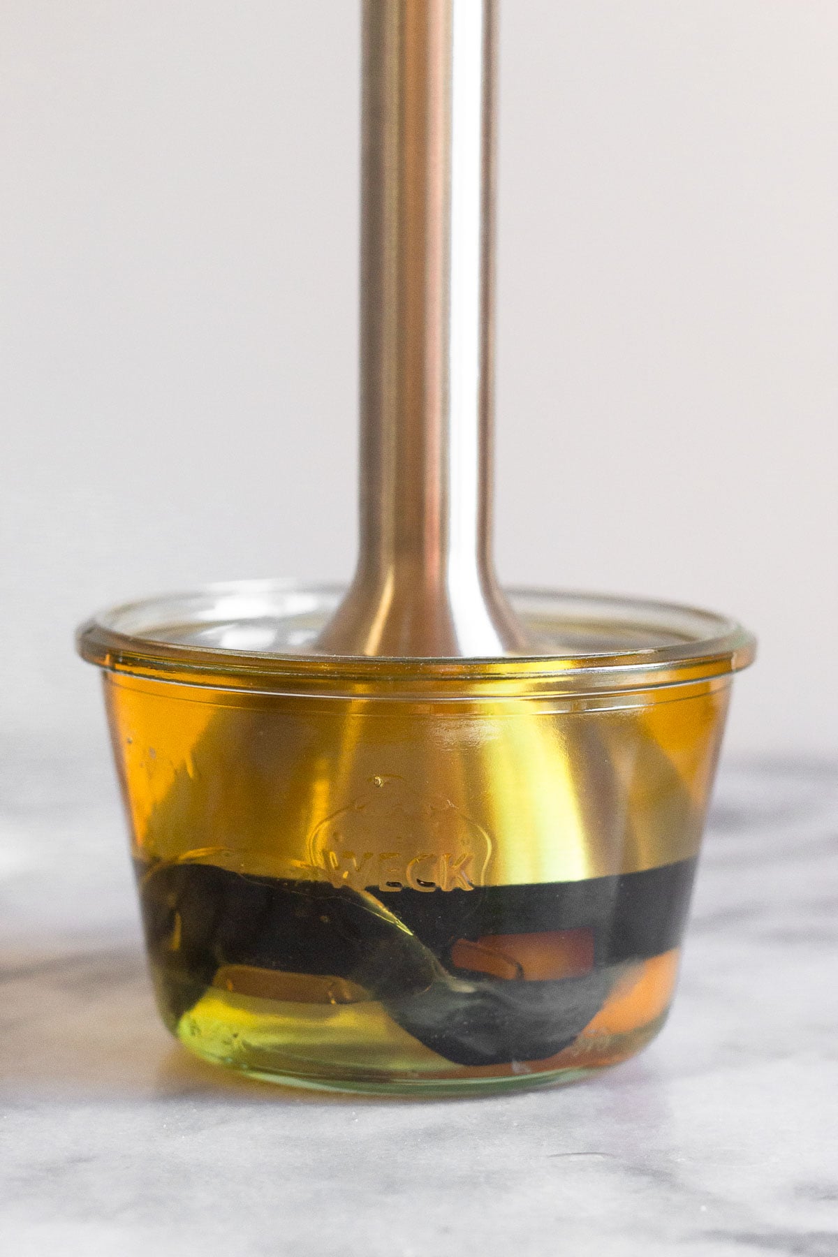 A small jar with oil and an egg with an immersion blender in it.