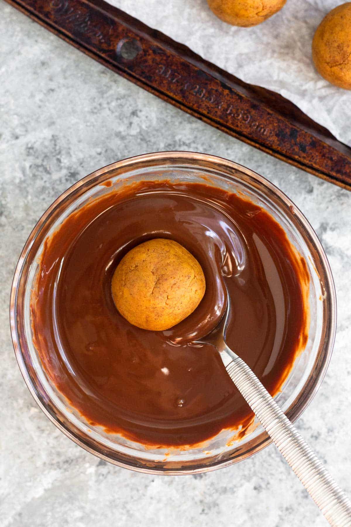 A ball of pumpkin cake pop batter on a spoon in a bowl of melted chocolate.