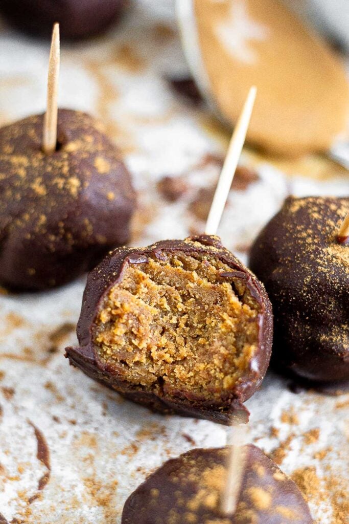 Close up of a protein cake pop with a bite taken out of it. Around it is more cake pops and a spoonful of peanut butter.
