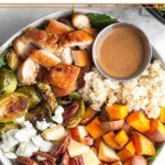 Sweetgreen harvest bowl with rice, roasted sweet potatoes, diced apples, pecans, goat cheese, roasted brussel sprouts, diced chicken, and small ramekin of creamy balsamic dressing over greens.