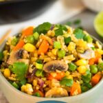 Small green bowl of broccoli fried rice topped with cilantro. Behind it is a large bowl of rice, half a lime, bowl of coconut aminos, and fresh ginger.