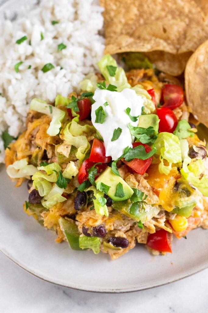 A close up of a piece of chicken taco casserole on a plate with tortilla chips and rice.