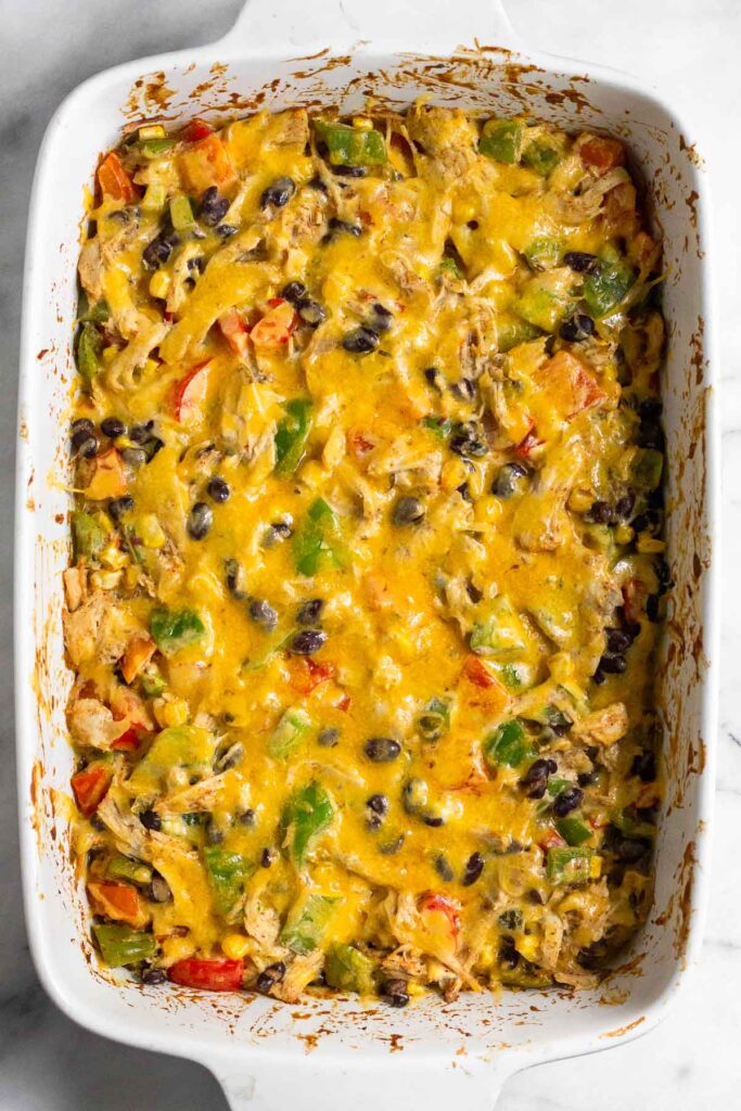 Cheesy chicken casserole with veggies and black beans topped with melted cheese in a large casserole dish.