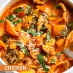 A bowl of chicken tomato soup topped with fresh herbs and cheese.