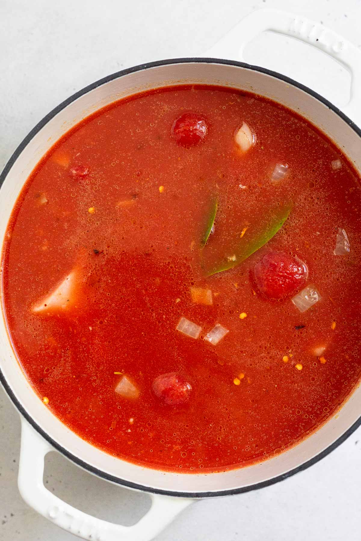 A large pot filled with broth, canned tomatoes, onions, and bay leaves.