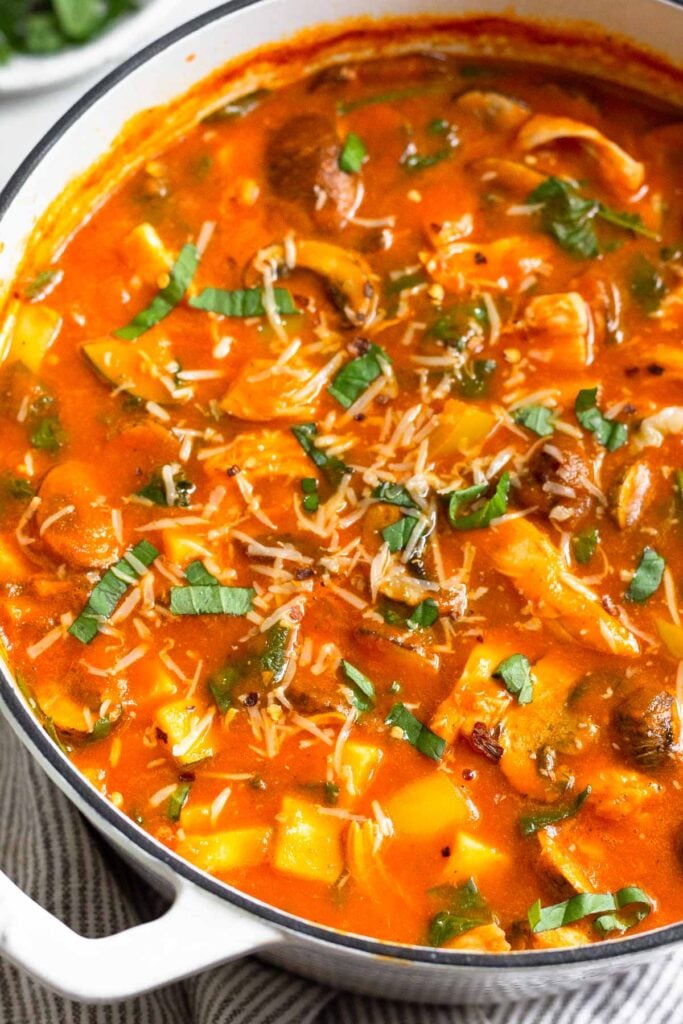 A large pot of creamy tomato soup with shredded chicken and veggies. It is topped with fresh basil and parmesan cheese.
