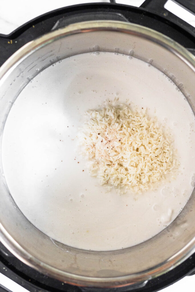 Pressure cooker filled with coconut milk with a pile of white rice in the middle of it.