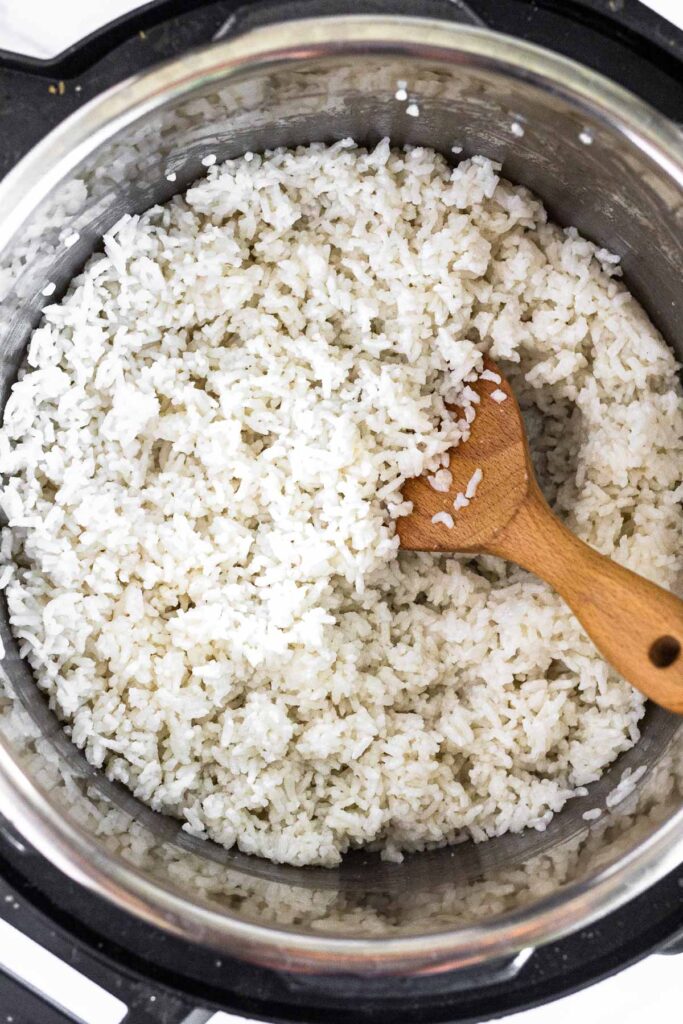 Instant pot filled with coconut rice with a wooden spoon in it.