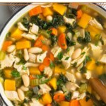 A large pot of leftover turkey soup with butternut squash, kale, veggies, and white beans.