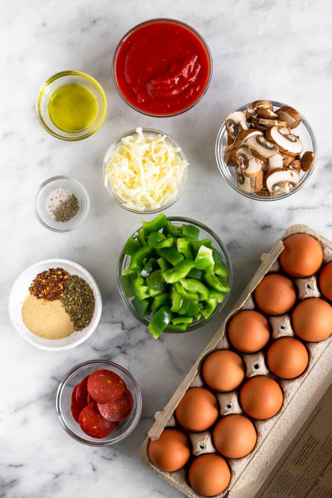 White counter with a bowl of pizza sauce, a bowl of sliced mushrooms, a carton of eggs, a bowl of pepperoni, a bowl of sliced peppers, a bowl of spice, a bowl of salt and pepper, a bowl of shredded cheese, and a bowl of oil.