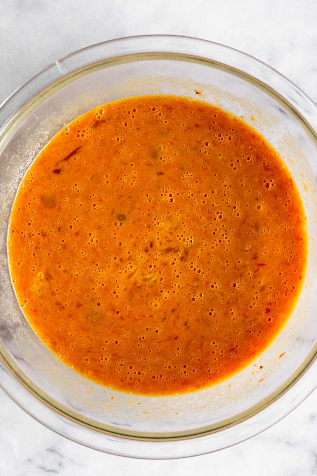 A bowl of whisked eggs mixed with red sauce.