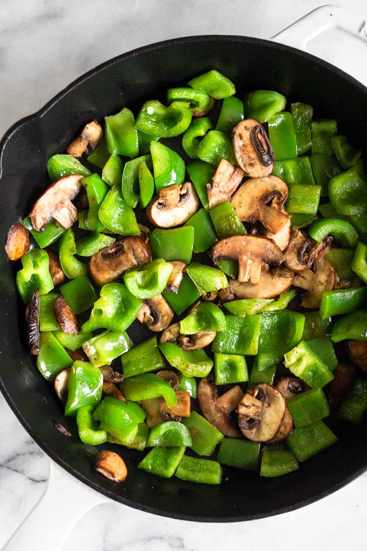 A skillet with sautéed green bell peppers and sliced mushrooms.