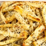 Roasted parsnips with crispy parmesan cheese and herbs on parchment paper on a wooden plate.