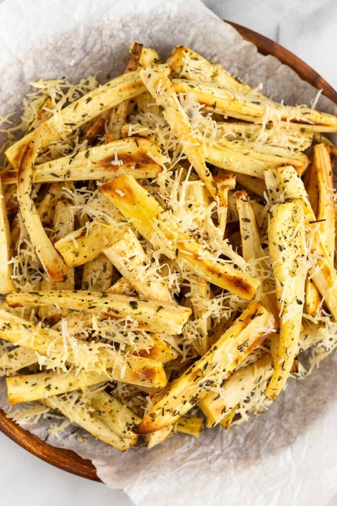 Overhead shot of parmesan roasted parsnips on wooden plate that is lined with parchment paper.