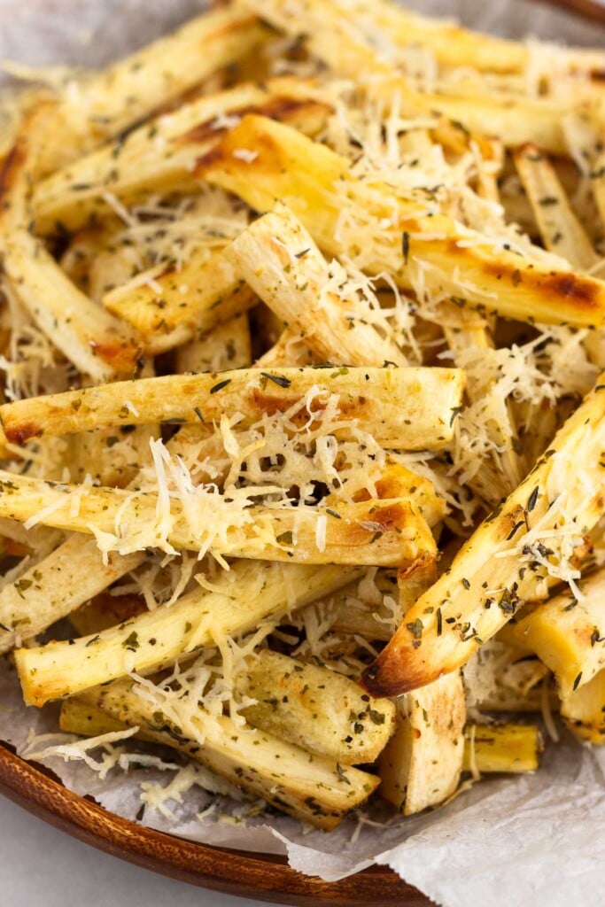 Close up of oven roasted parsnips with parmesan cheese and herbs on a plate.