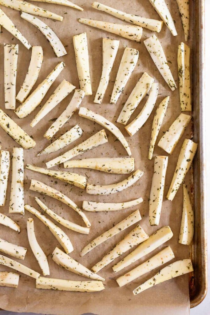 Baking sheet filled with parsnips that have been cut into matchsticks tossed with oil and spices.