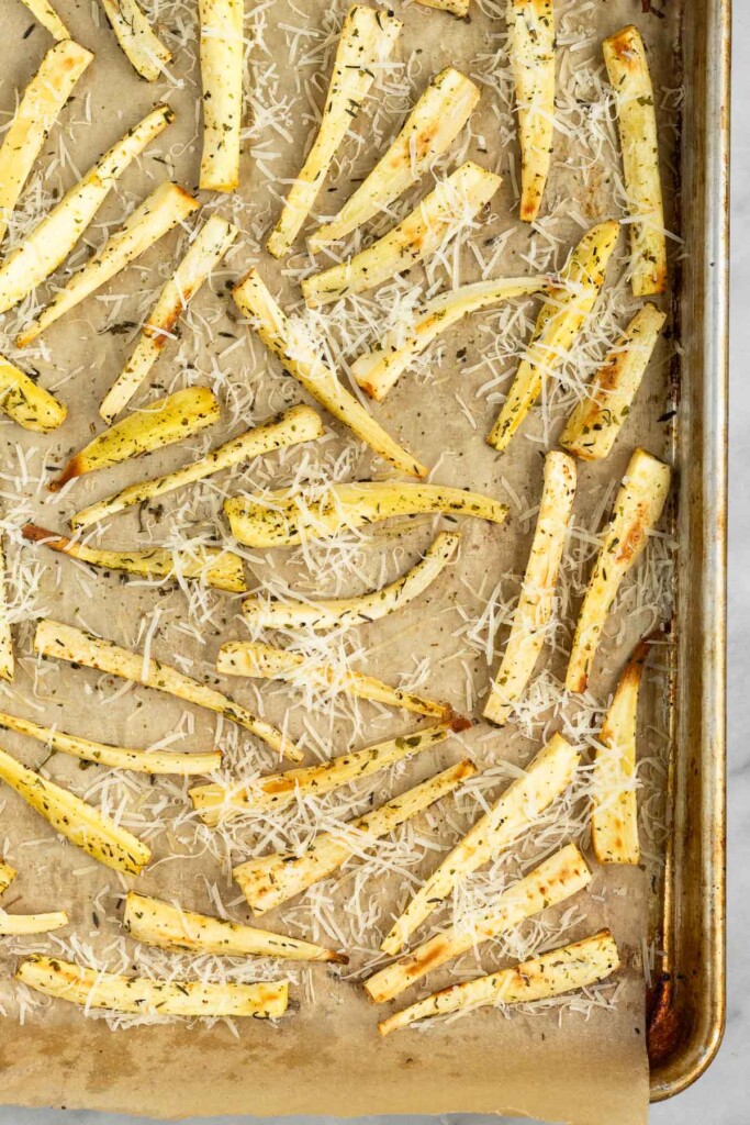 A baking sheet filled with parsnips that have been roasted and are covered with parmesan cheese.