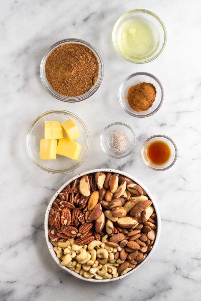 White counter top with a bowl of egg whites, a bowl of spices, a bowl of vanilla extract, a bowl of mixed nuts, a bowl of salt, a bowl of sugar, and bowl of coconut sugar.