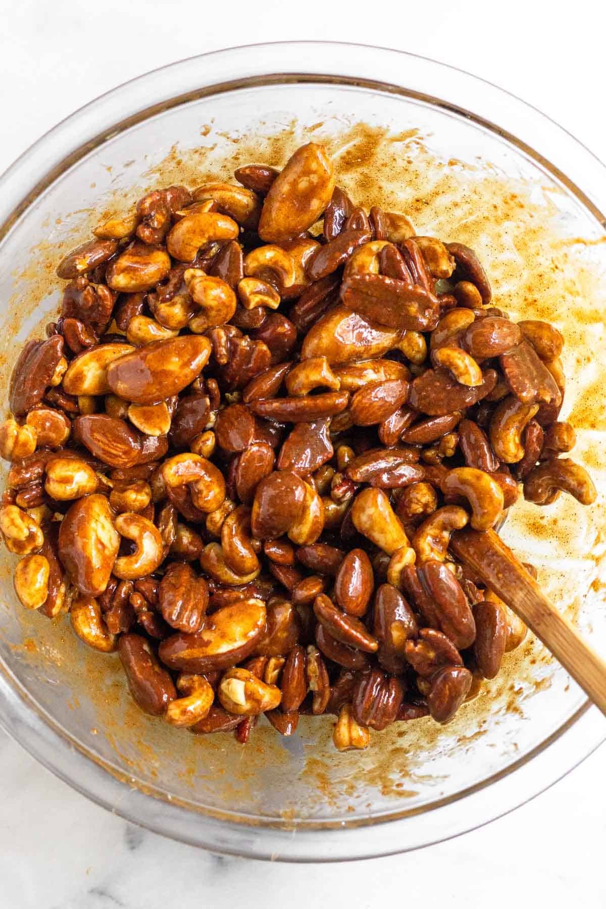 Glass bowl filled with mixed nuts coated in a sticky sugar mixture.