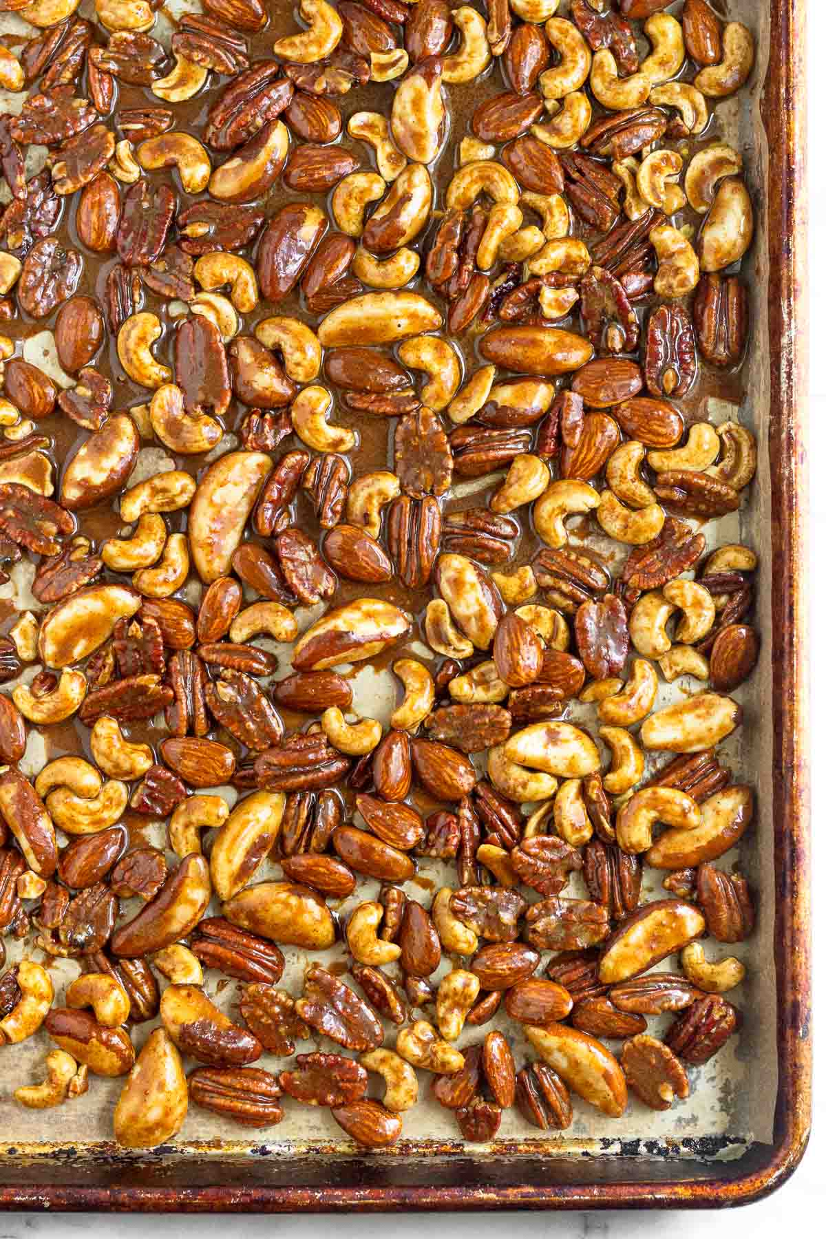 Baking sheet filled with mixed nuts coated in a sugar mixture before baking.