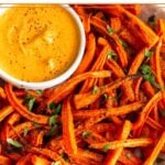 Baked carrot fries in bowl topped with cilantro. Also in the bowl is small ramekin of curry dipping sauce.