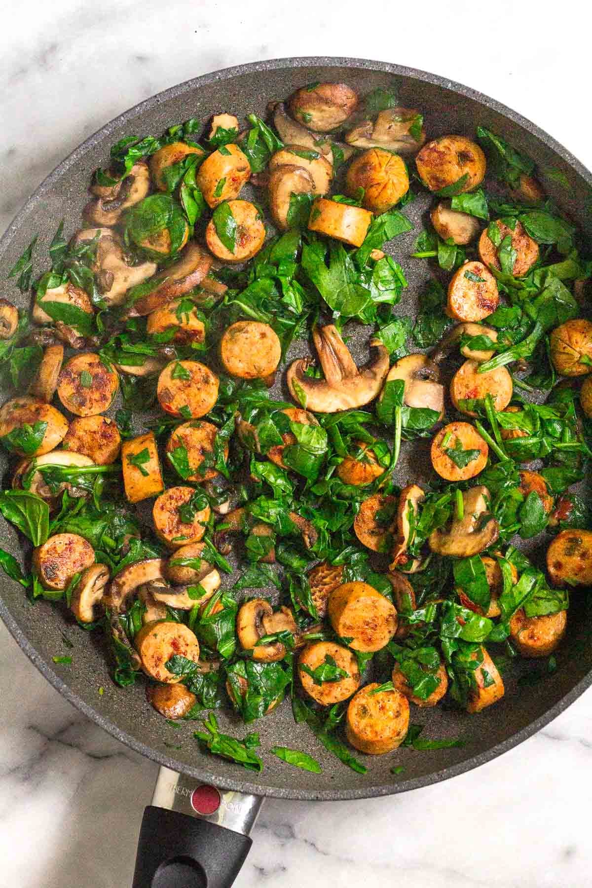 Saute pan filled with sautéed chicken sausage, mushrooms, and spinach.