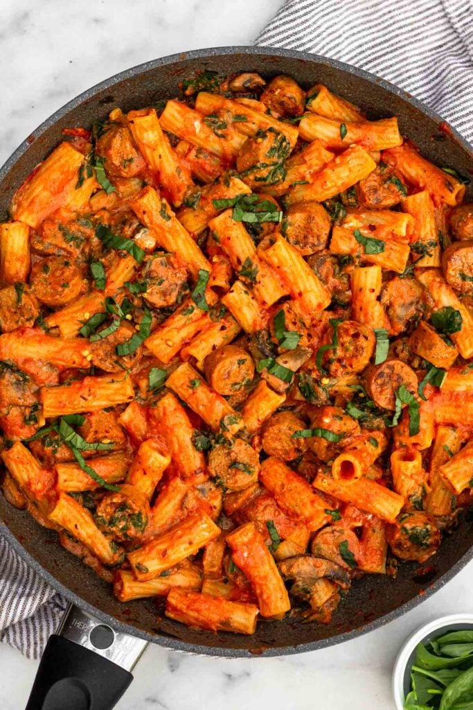 Pasta with chicken sausage, spinach, mushrooms, and marinara sauce in a large skillet. It stopped with fresh basil. A small ramekin of basil is next to the skillet.