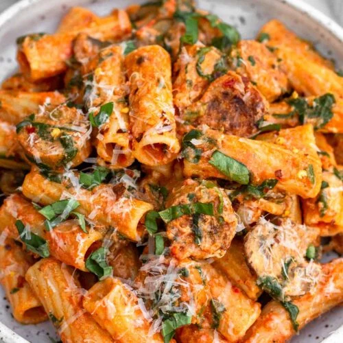 Chicken sausage pasta on a plate topped with basil and parmesan cheese.